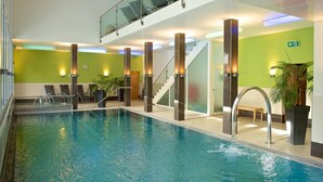 Una piscina interior con agua cristalina, rodeada de barandillas de vidrio y pilares modernos.
