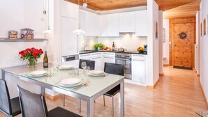 Una cocina moderna con armarios blancos, una isla central y un comedor con mesa de vidrio.
