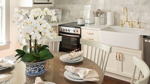 A modern kitchen with white cabinets, a marble backsplash, a built-in oven, and a dining area with a glass table and chairs. - Newly Restored Historic Home, Close to King! (Charleston)