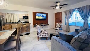 Ein modernes Wohnzimmer mit Flachbildfernseher, Deckenventilator und großem Fenster mit Vorhängen.