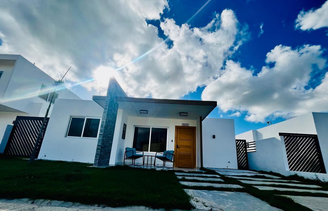 Una casa moderna con fachada blanca, una puerta de madera y un pequeño patio con dos sillas.