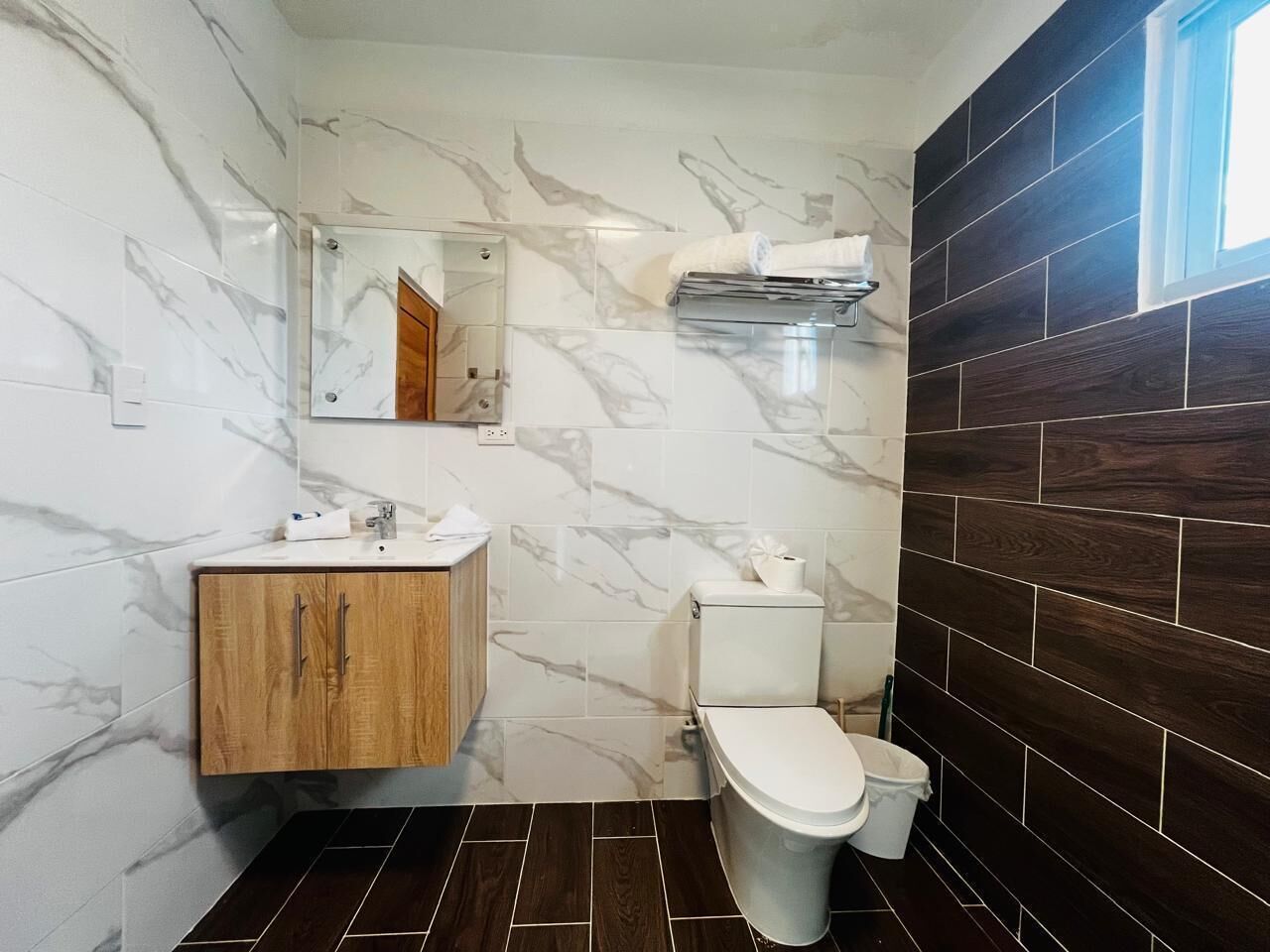 A bathroom with a marble wall, a wooden cabinet, a toilet, and a dark wood panel wall.