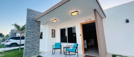 Une maison moderne dotée d’un patio comprenant deux chaises bleues et une petite table.