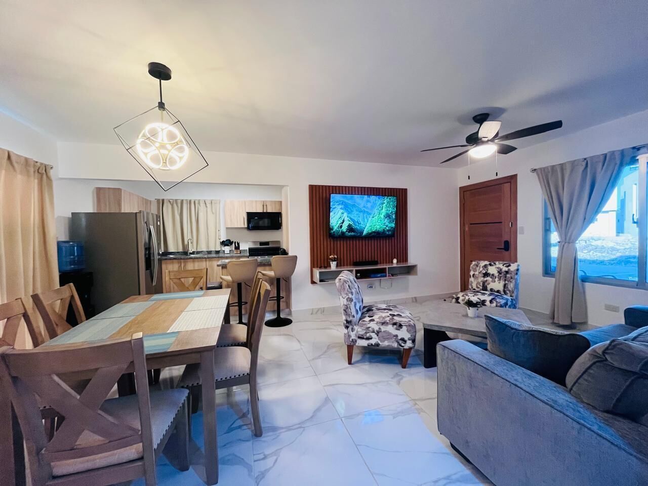 Un salon moderne comprenant un coin repas, un téléviseur fixé au mur et un ventilateur de plafond.