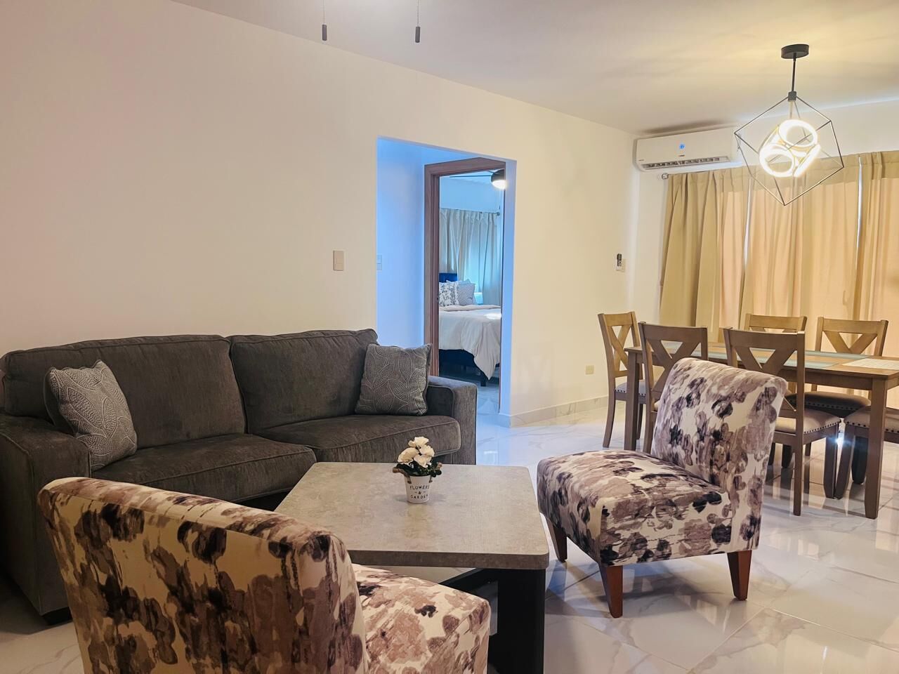 Una sala de estar con un sofá, dos sillones, una mesa de centro y un comedor con mesa y sillas.