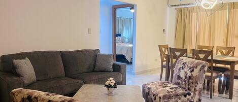 Una sala de estar con un sofá, dos sillones, una mesa de centro y un comedor con mesa y sillas.