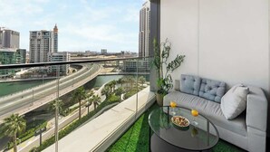 Un balcon moderne avec un canapé et une table en verre, offrant une vue sur un paysage urbain avec une rivière et des routes.