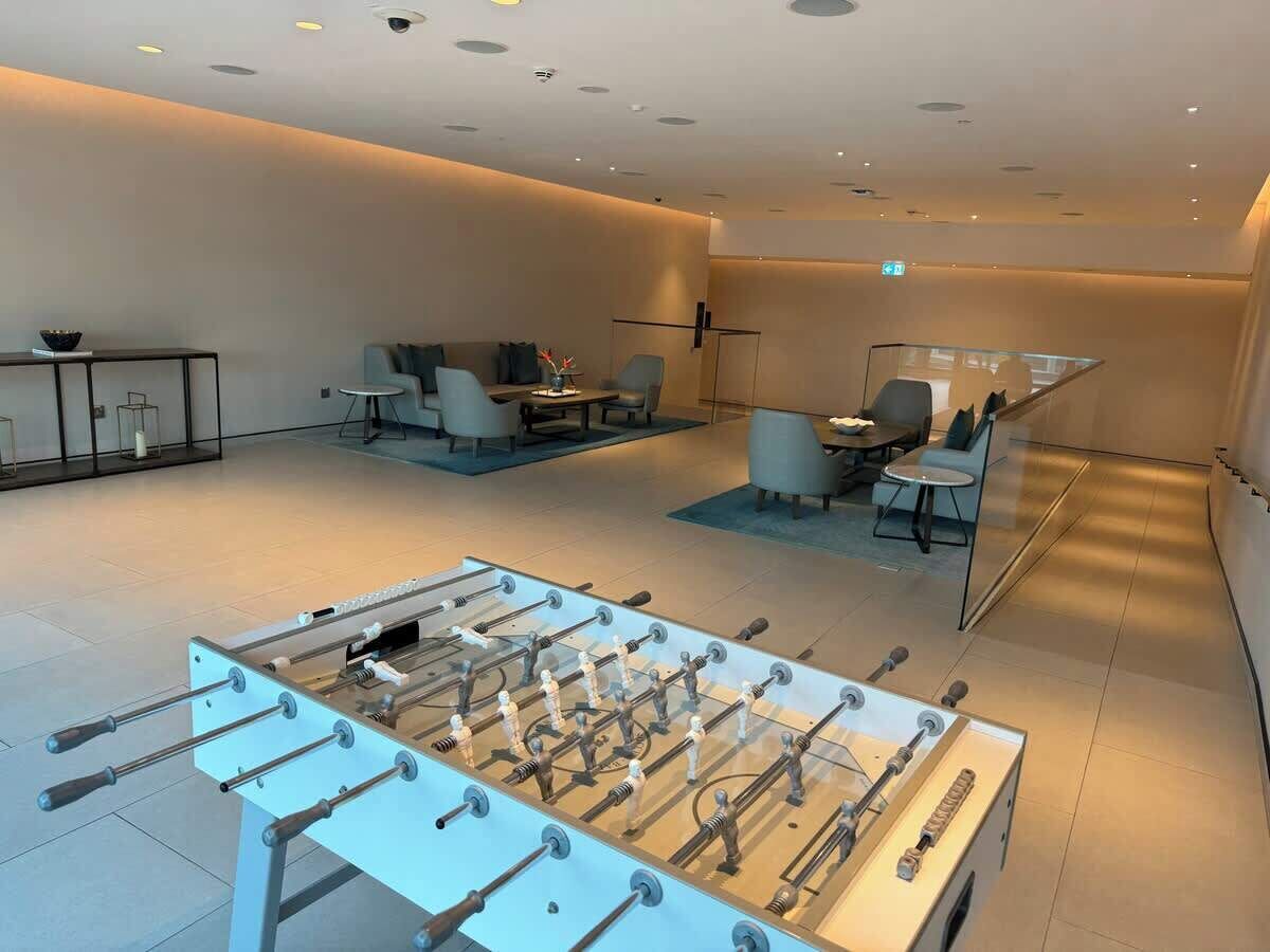 A modern indoor space with a foosball table, seating area, and a glass partition.