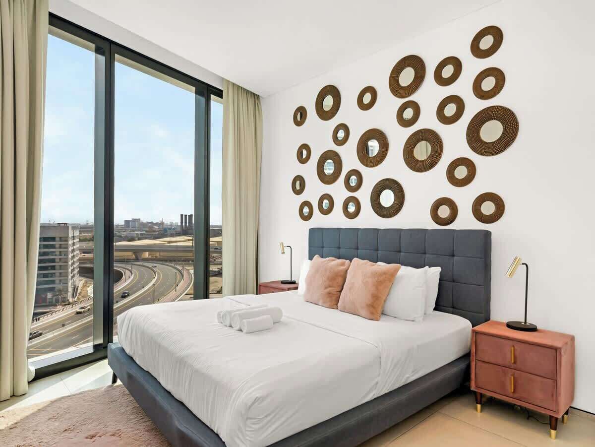 A modern hotel room with a large bed, a view of a highway, and a wall decorated with circular mirrors.