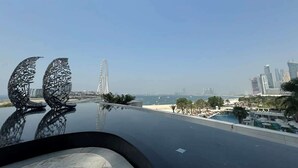 Une piscine sur le toit, agrémentée de deux sculptures métalliques abstraites, d’une grande roue et d’un panorama urbain avec des gratte-ciel en arrière-plan.