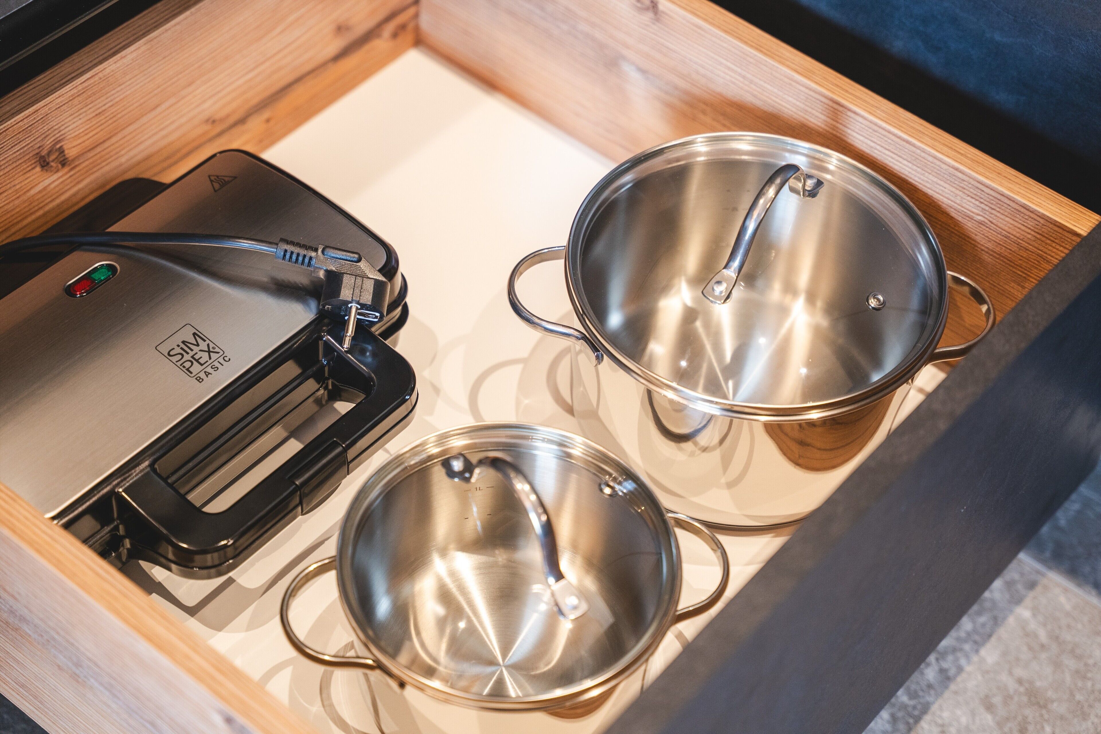 Un cajón de cocina con un procesador de alimentos, dos ollas de acero inoxidable y un recipiente negro para utensilios.