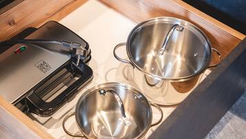 Un cajón de cocina con un procesador de alimentos, dos ollas de acero inoxidable y un recipiente negro para utensilios.