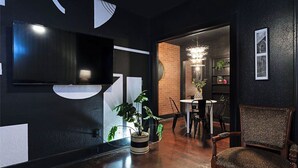 A modern living room with a flat-screen TV, a dining area with a brick wall, and a chandelier. - 2BR The Montrose Serenity APT! Stroll & Relax ★★★★★ (Houston)