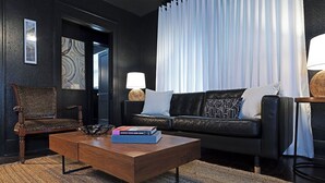 A modern living room with a dark leather sofa, a wooden coffee table with a book, a wicker chair, and a lamp. - 2BR The Montrose Serenity APT! Stroll & Relax ★★★★★ (Houston)