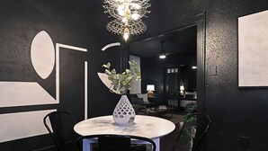 A modern dining area with a round table, black chairs, a white vase with flowers, and a unique geometric light fixture. - 2BR The Montrose Serenity APT! Stroll & Relax ★★★★★ (Houston)