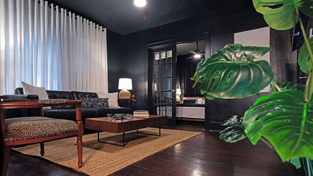 A modern living room with a dark wood floor, a leather sofa, a coffee table, and a large plant. - 2BR The Montrose Serenity APT! Stroll & Relax ★★★★★ (Houston)