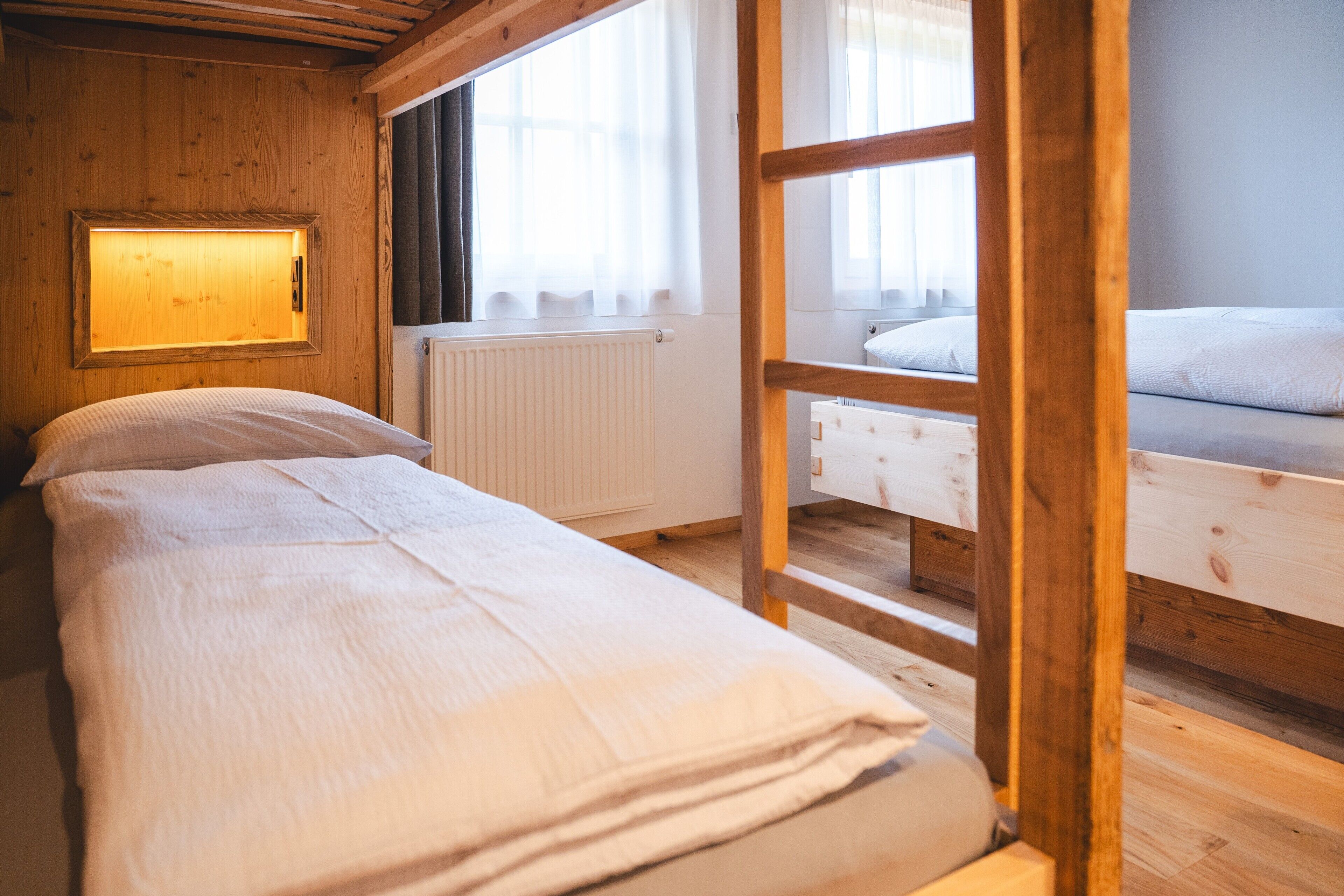 Een houten kamer met een bed, een raam met gordijnen, een radiator en een houten ladder.