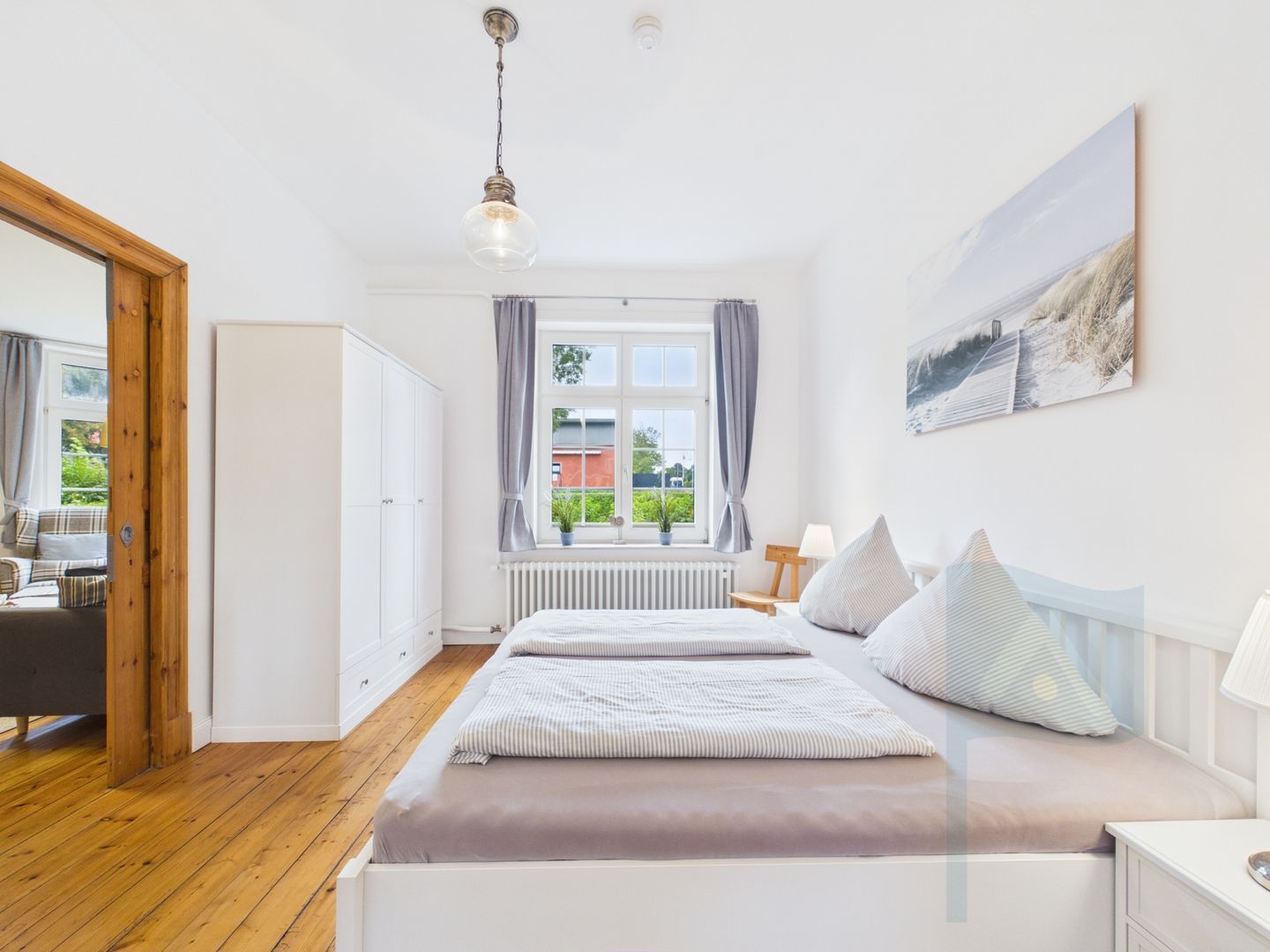 A bedroom with a bed, a window with curtains, a radiator, and a painting on the wall.