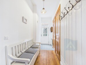 A hallway with a white bench, wooden flooring, a hanging light fixture, and a door with a window.