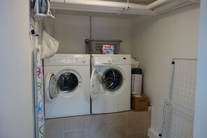 Uma área de lavanderia com duas máquinas de lavar frontais, uma caixa de detergente Persil e um varal.