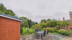 Eine Terrasse mit Ziegelmauer, Tisch mit Stühlen und ein Garten mit Zaun.