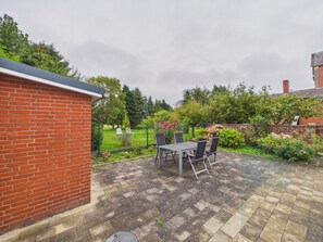 Eine Terrasse mit Ziegelmauer, Tisch mit Stühlen und ein Garten mit Zaun.