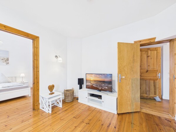 A room with a bed, a TV on a stand, a small table with a lamp, and a wooden door.