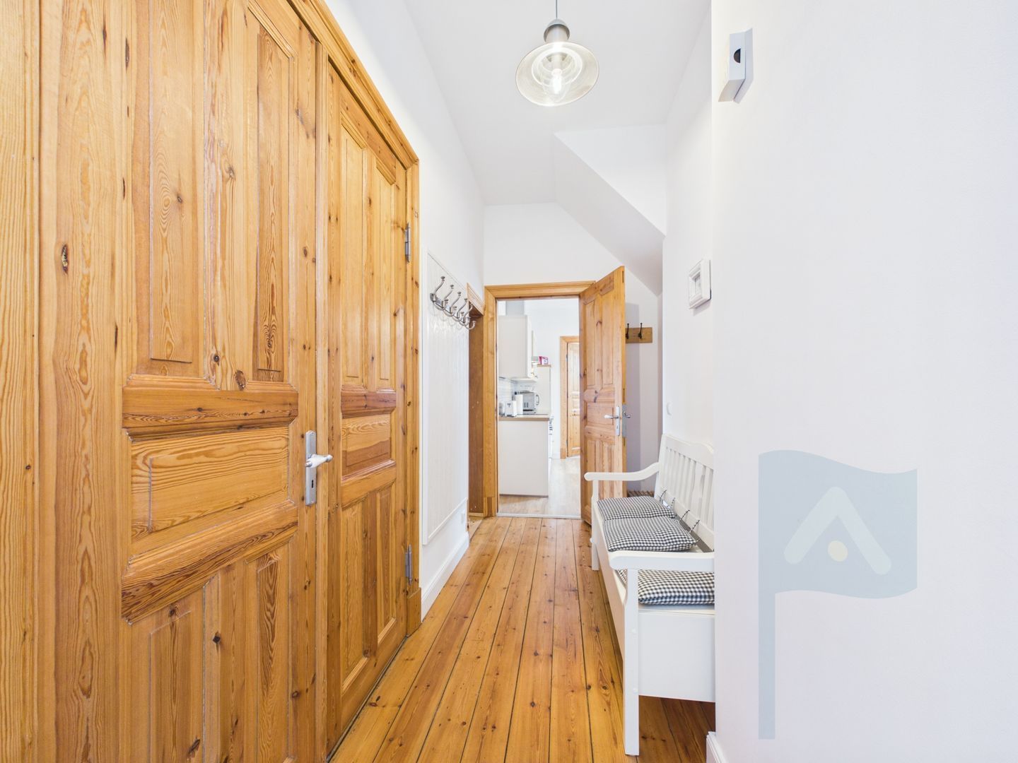A hallway with wooden doors, a bench, and a kitchen area in the background.