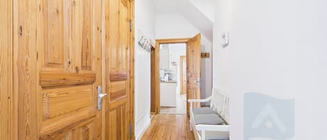 A hallway with wooden doors, a bench, and a kitchen area in the background.