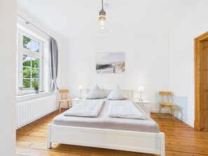 A bedroom with a bed, bedside tables, a lamp, a window, and a painting on the wall.