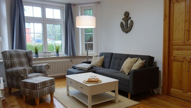 Ett mysigt vardagsrum med en fåtölj i rutigt tyg, en mörk soffa och ett vitt soffbord.