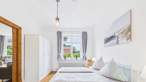 Ein Schlafzimmer mit einem Bett, einem Fenster mit Vorhängen, einem Heizkörper und einem Bild an der Wand.