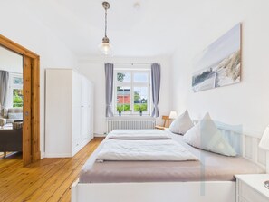Ein Schlafzimmer mit einem Bett, einem Fenster mit Vorhängen, einem Heizkörper und einem Bild an der Wand.