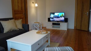 Ett vardagsrum med en vit soffa, ett soffbord, en tv på ett vitt tv-bord och trägolv.