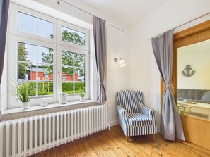 A room with a large window, a radiator, a striped chair, and a wall-mounted light fixture.