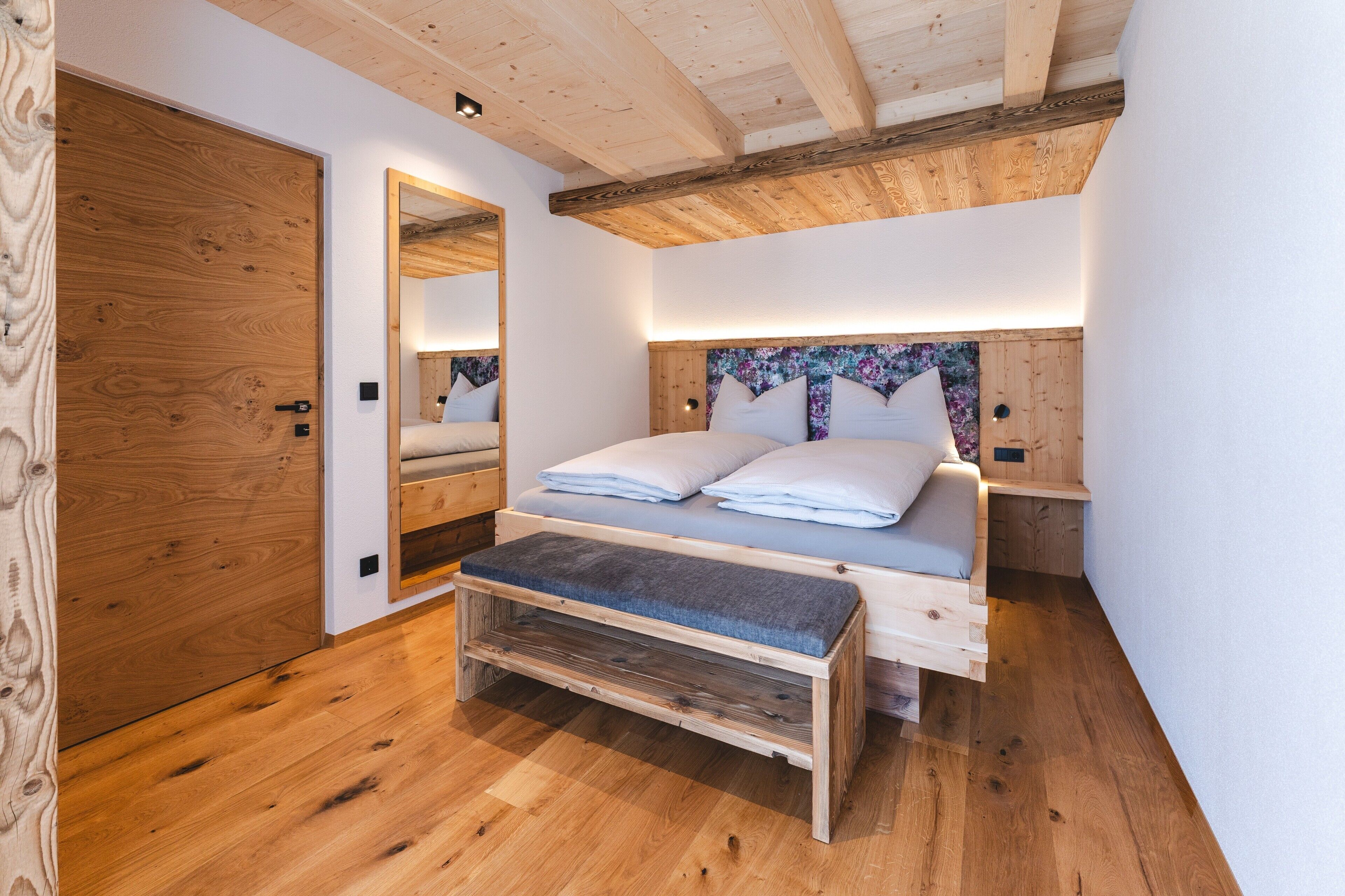 Ein Schlafzimmer mit einem hölzernen Bett, einer Bank, einem Spiegel und einer Holzzahl.