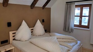 A bedroom with a wooden headboard, a bedside table, a window with curtains, and a view of the outside.