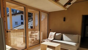 A room with a sliding glass door leading to a balcony, a sofa, a small table, and a television.