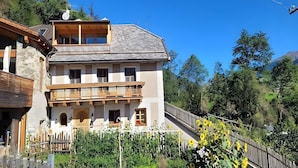 A two-story building with a balcony, a wooden fence, and a garden with sunflowers.