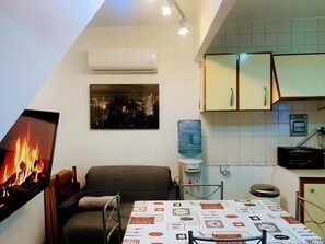 Et kompakt køkken med en vanddispenser, en ovn med ildvisning og et spiseområde med et bord dækket til to.