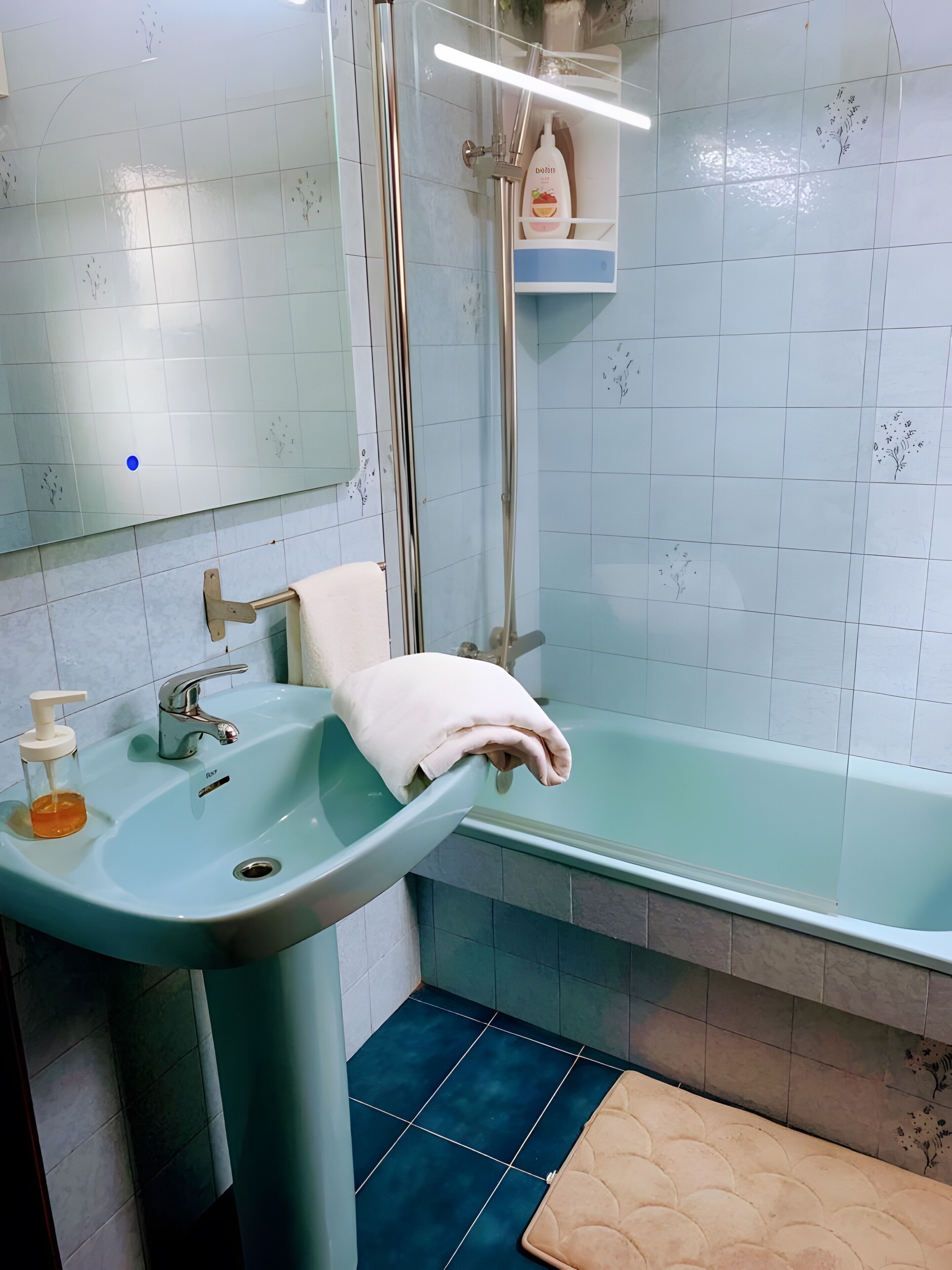 A bathroom with a sink, mirror, shower, and a towel rack.
