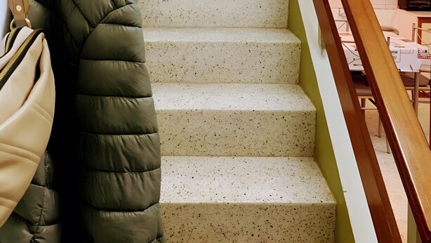 Una escalera con barandilla de madera, escalones color beige y pared verde.