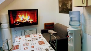 Una habitación pequeña con una televisión mostrando una chimenea, un dispensador de agua y una mesa con mantel.