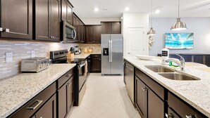 A modern kitchen with dark cabinets, stainless steel appliances, and a granite countertop. - Brand New Home at Windsor Cay Resort with Lazy River (Clermont)