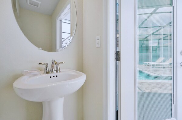 A bathroom with a white sink, a mirror, and a window with blinds.