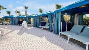 A poolside area with blue canopies, lounge chairs, and a paved walkway. - Brand New Home at Windsor Cay Resort with Lazy River (Clermont)