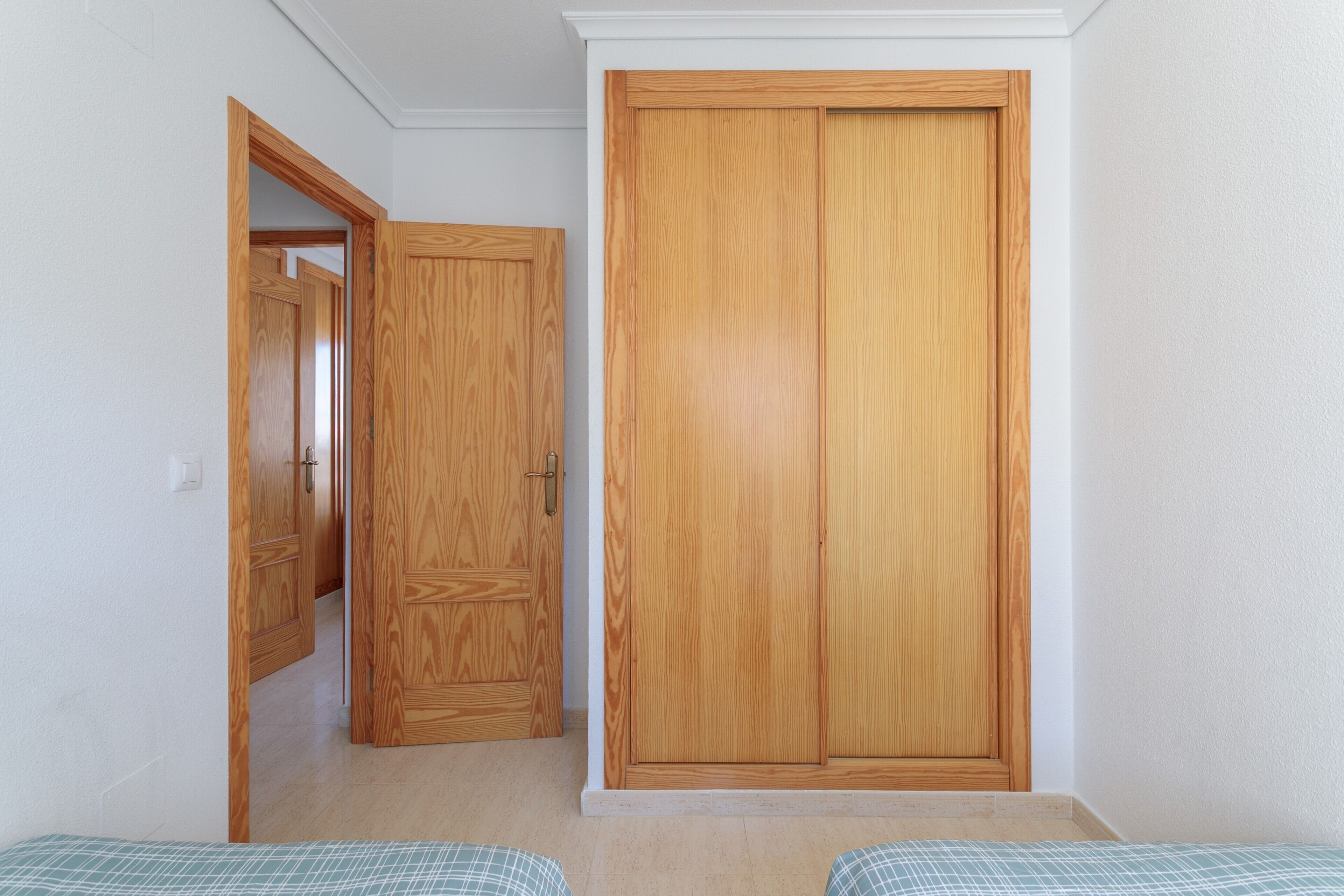 A room with a wooden wardrobe, a bed with a checkered bedspread, and a white wall.