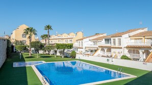 A swimming pool surrounded by a well-maintained lawn, with buildings featuring traditional architecture in the background. - Holiday Home 'Horizon Oasis' with Sea View, Wi-Fi and Air Conditioning (Santa Pola)