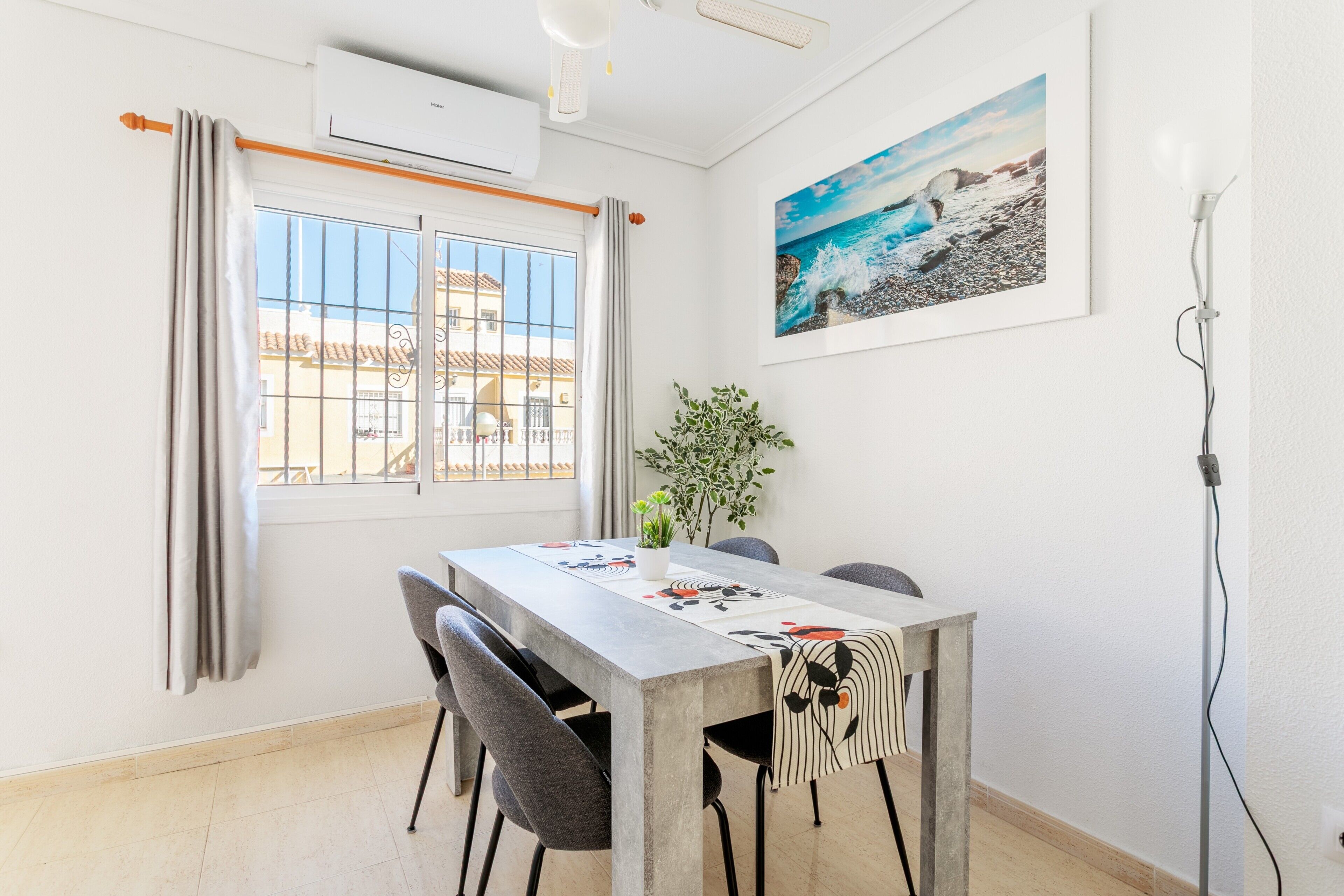 Un comedor con una mesa, sillas, una planta en maceta y un cuadro en la pared.