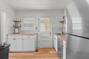 Eine moderne Küche mit weißen Schränken, einer Holzarbeitsplatte, einem Edelstahlkühlschrank und einem Geschirrspüler.